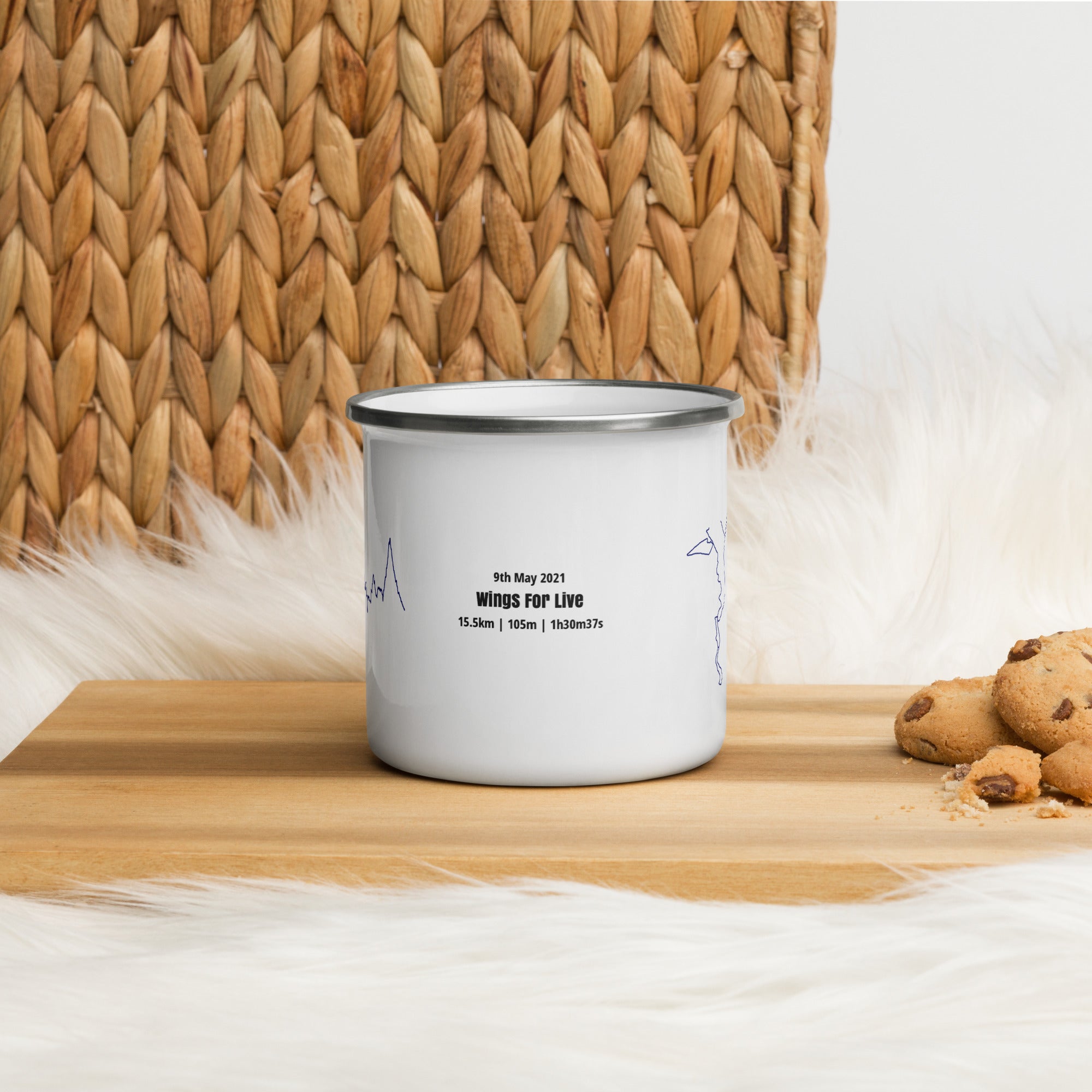 White enamel mug with text and custom Strava route print on a wooden surface with cookies and a woven basket in the background