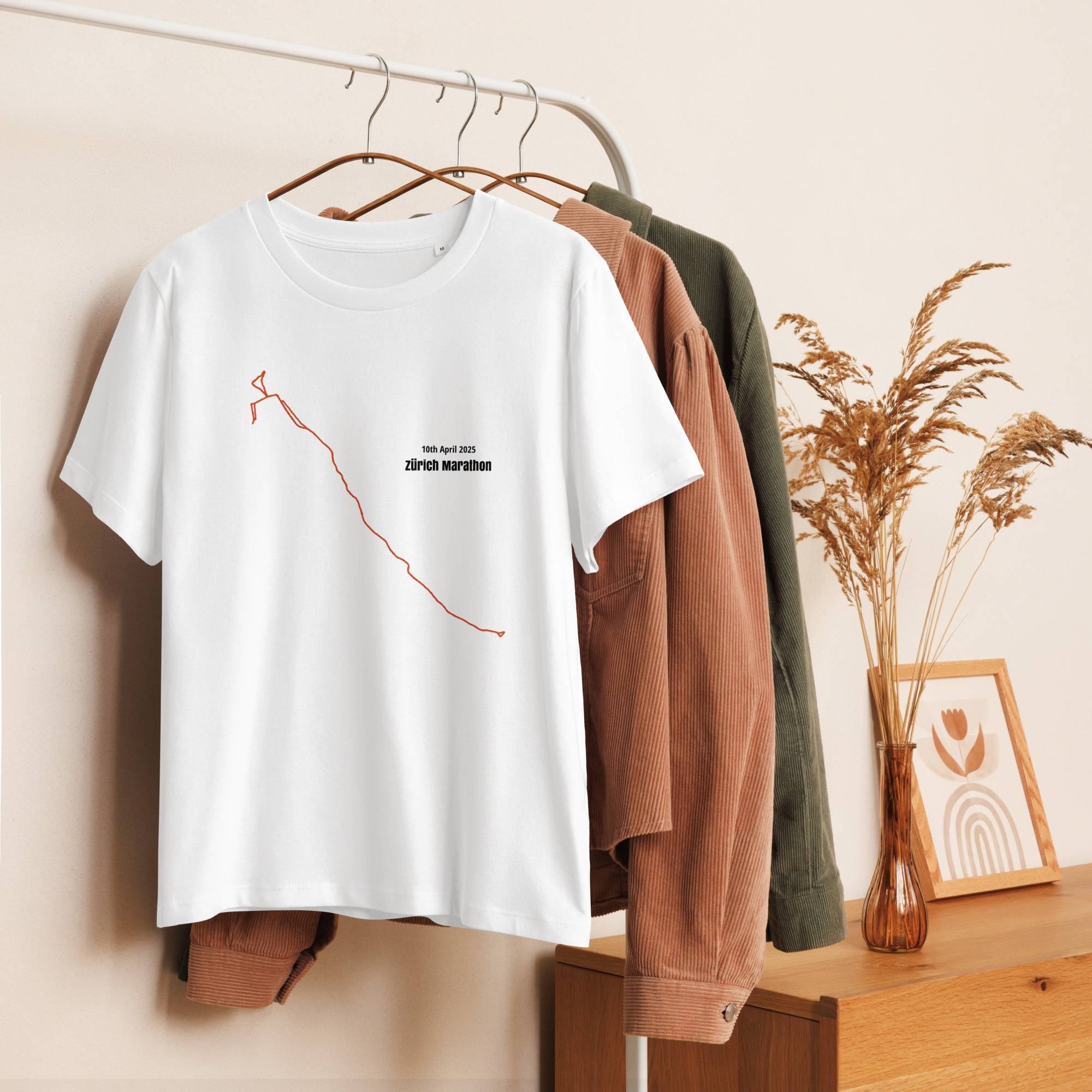 White t-shirt with a custom Strava route print design on a hanger against a neutral wall with clothes and decor