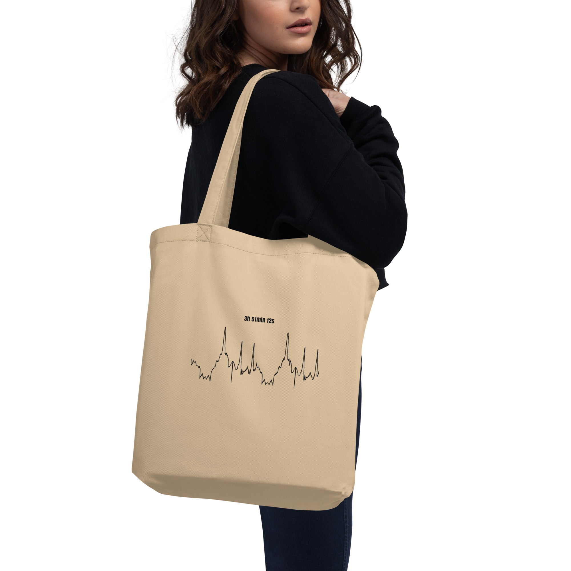 Beige tote bag with a black custom Strava route print art design held by a person on a white background