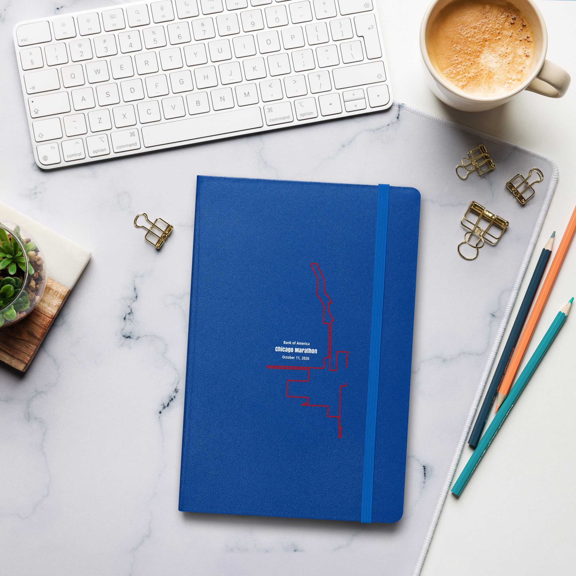 Blue notebook with a custom Strava route print art design on a marble desk with office supplies and a cup of coffee