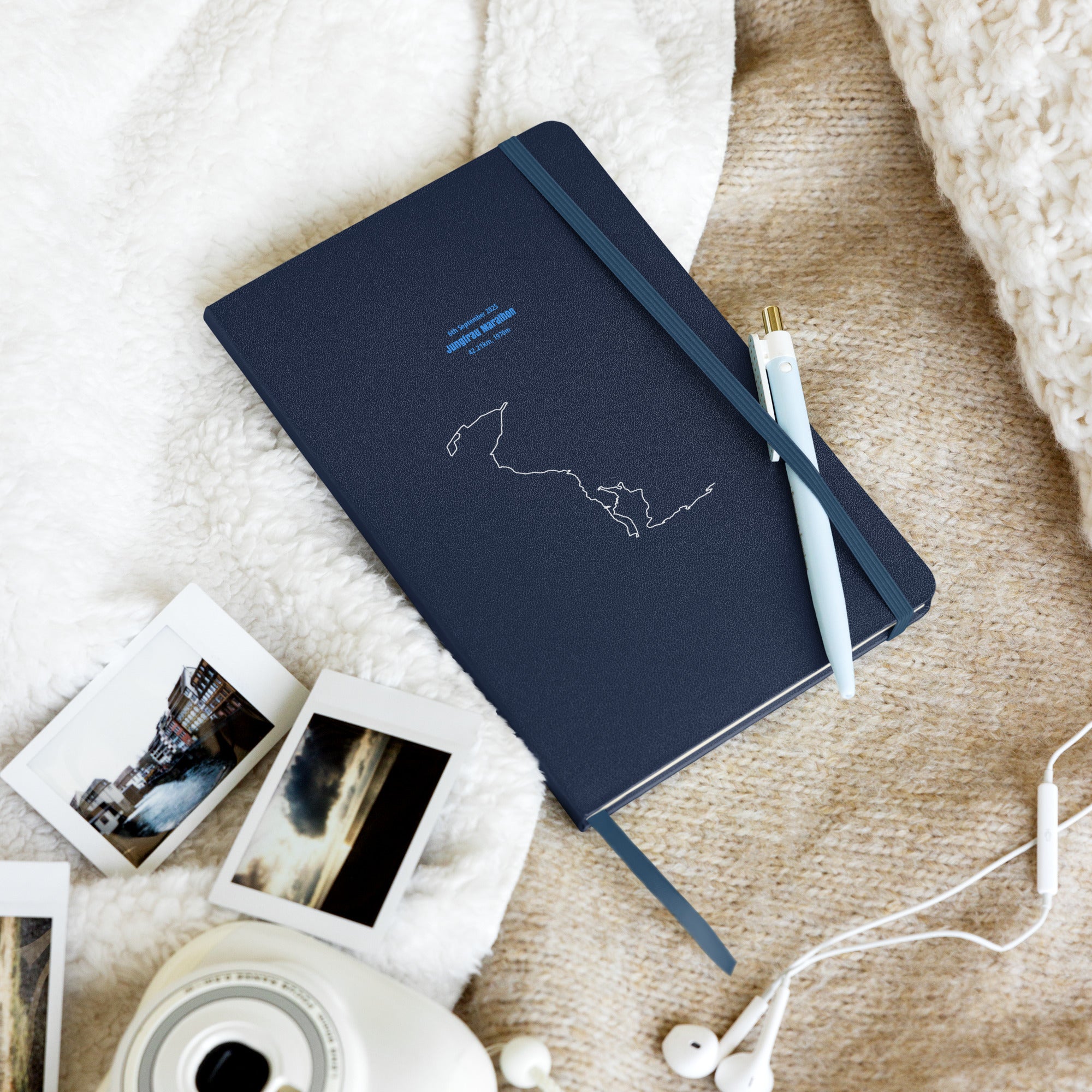 Dark blue notebook with custom Strava route print art design on a textured surface with photos and earphones