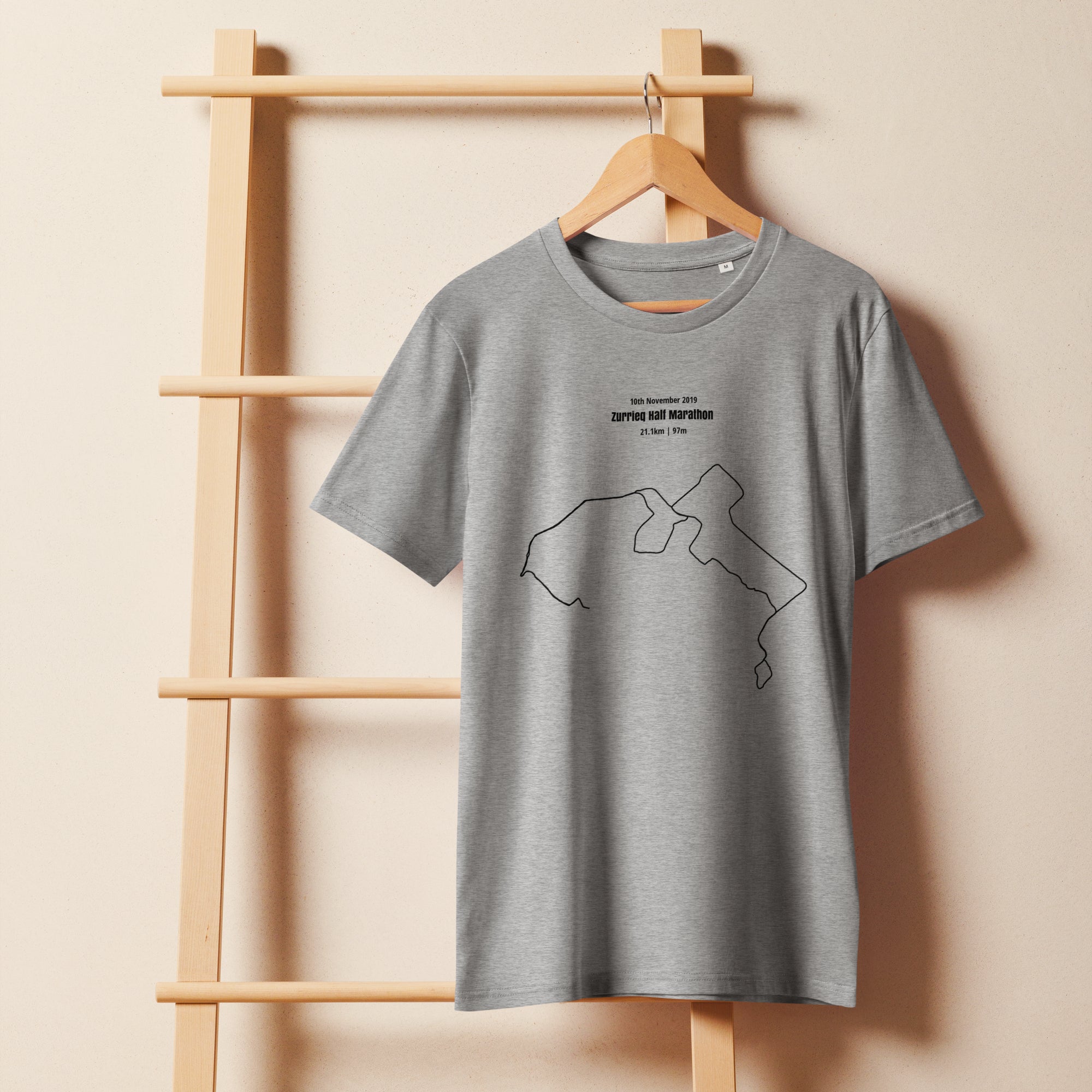 Gray t-shirt with a custom Strava route print art design on a wooden hanger against a beige wall