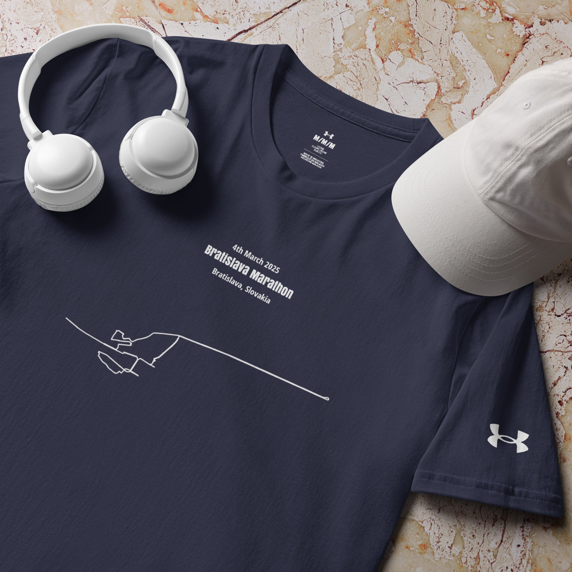 Navy blue t-shirt with white text and custom Strava route print design, accompanied by white headphones and cap on a textured surface