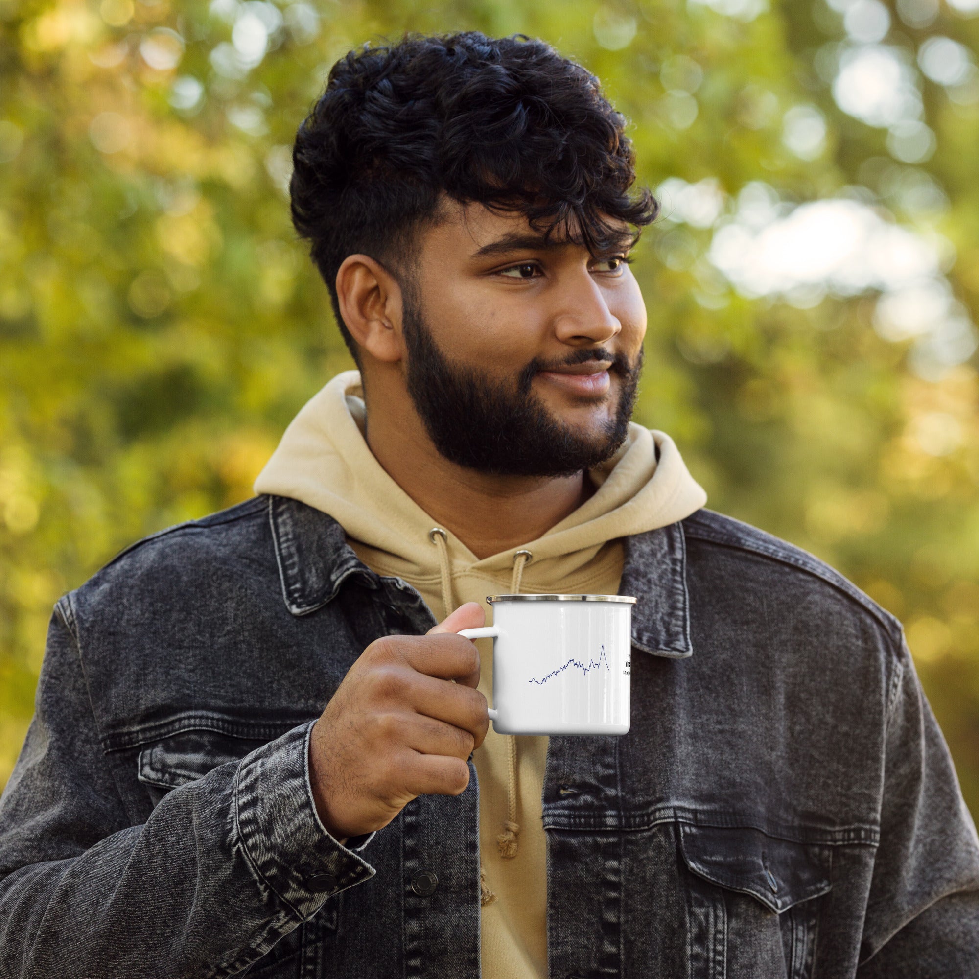 Man holding a metal mug with custom Strava route print outdoors with greenery in the background