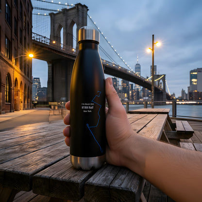 Hand holding a black insulated bottle with a custom Strava print art and cityscape and bridge in the background
