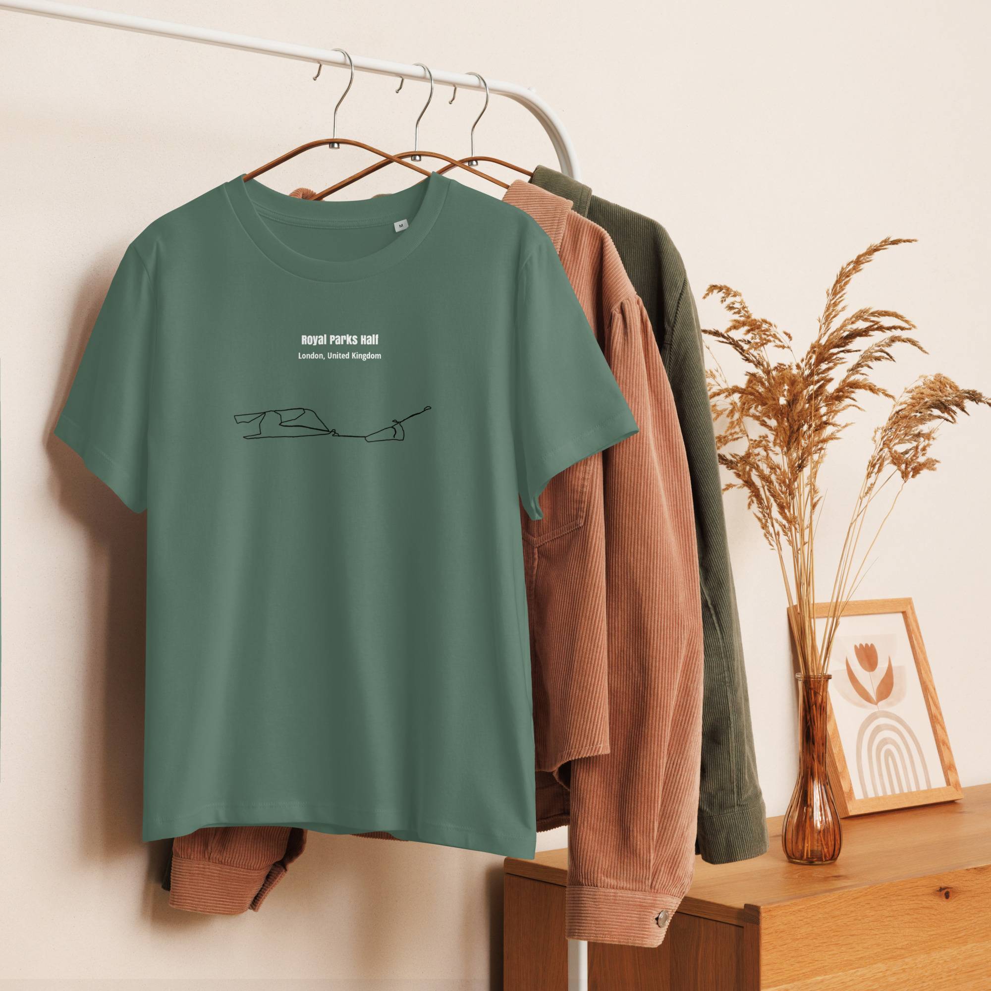 Green t-shirt with text and custom Strava route print on a hanger against a neutral wall with a wooden surface and plant