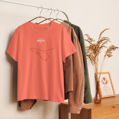 Coral t-shirt with a custom Strava route print design on a hanger against a neutral wall with a wooden surface