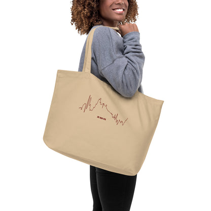 Person holding a beige tote bag with custom Strava route print art on a white background