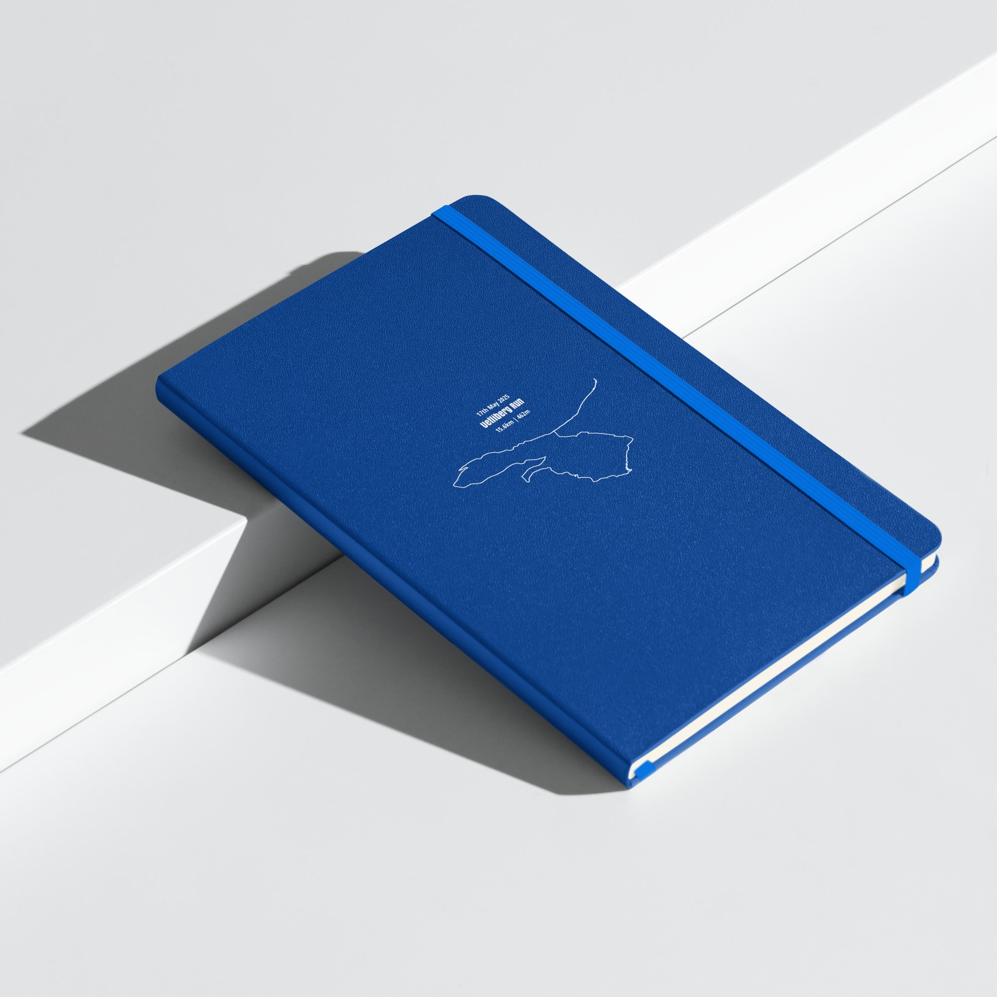 Blue notebook with a white custom Strava route print art on a light gray background