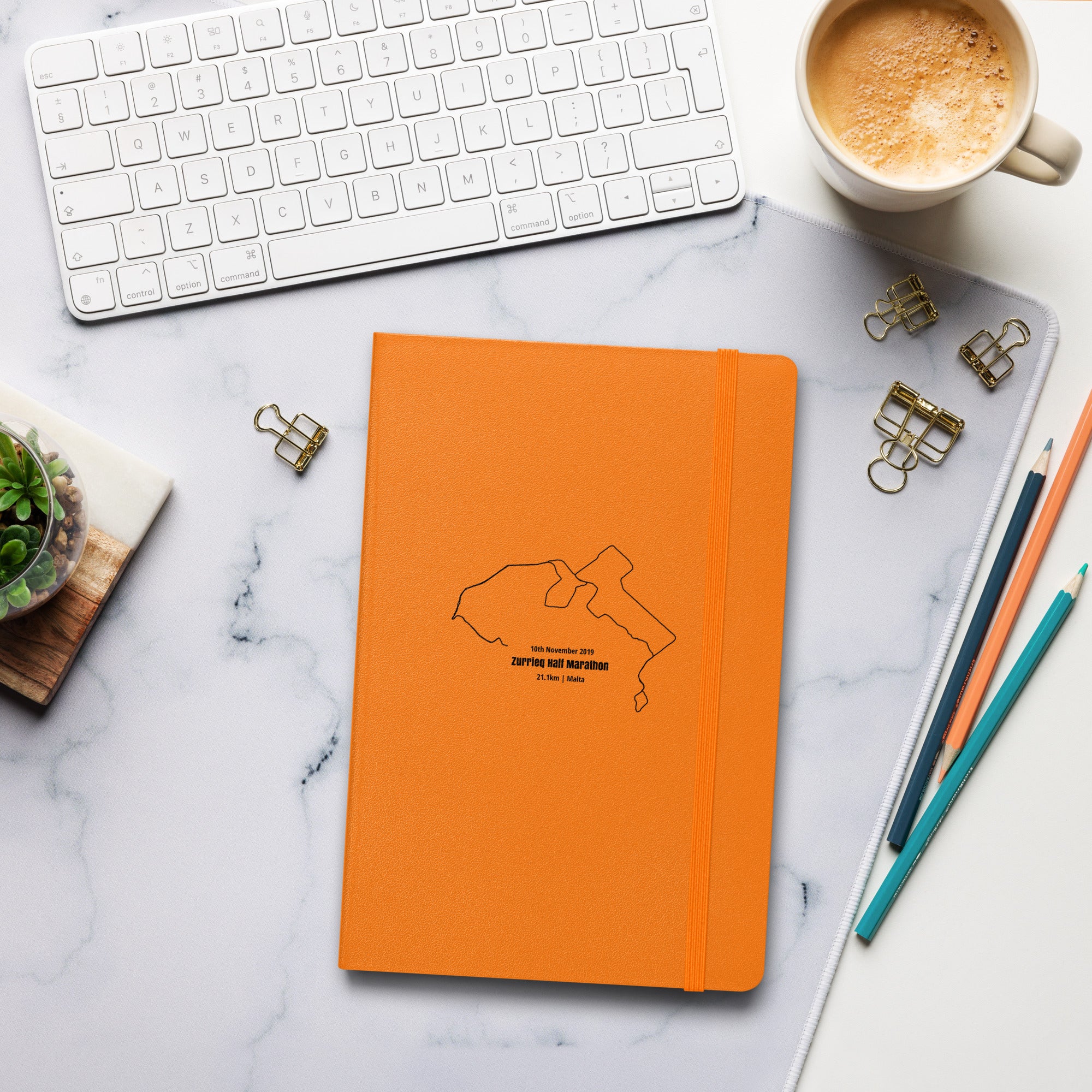 Orange notebook with custom Strava route print art design on a marble desk with office supplies and a cup of coffee