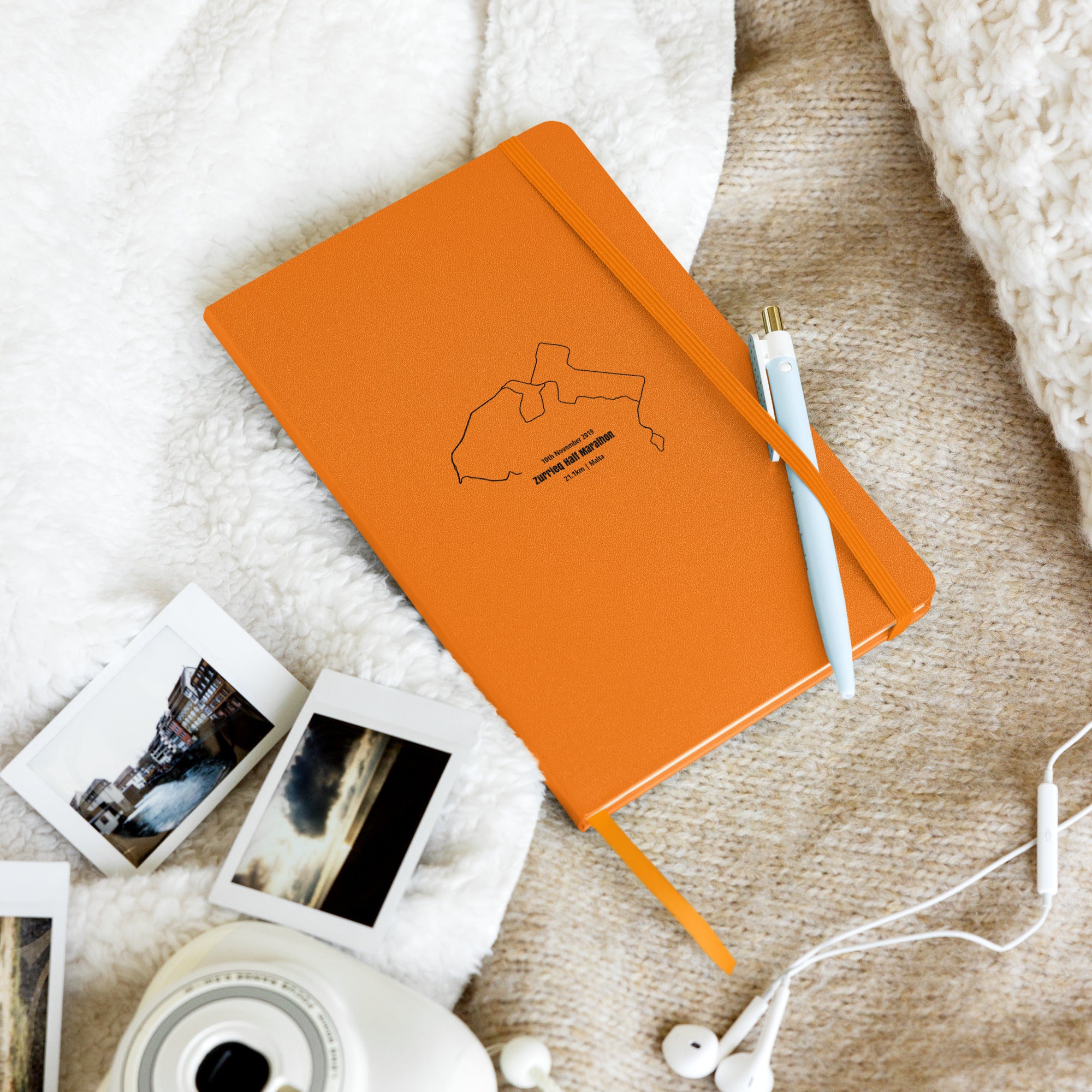 Orange notebook with custom Strava route print art on a textured surface with photos and earphones