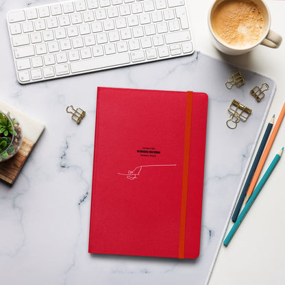 Red notebook with custom Strava route print art and an orange strap on a marble desk with office supplies and a cup of coffee