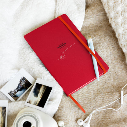 Red notebook with custom Strava route print art and a white pen on a textured surface with photos and earphones