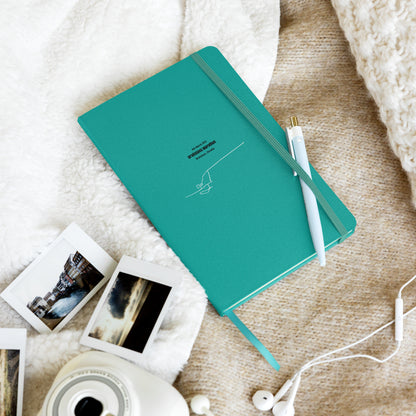 Teal notebook with custom Strava route print art and a pen on a textured surface with photos and earphones
