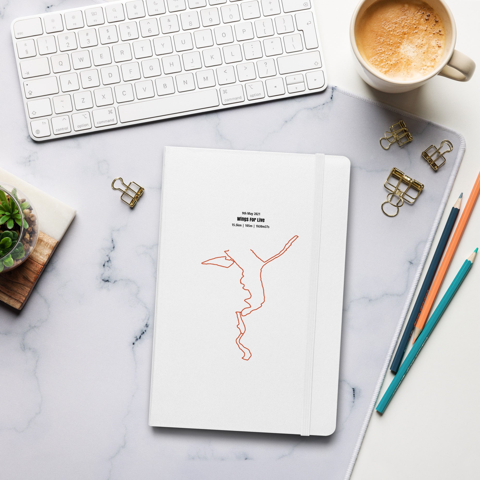 Notebook with custom Strava route print art on a marble desk with a keyboard and coffee cup