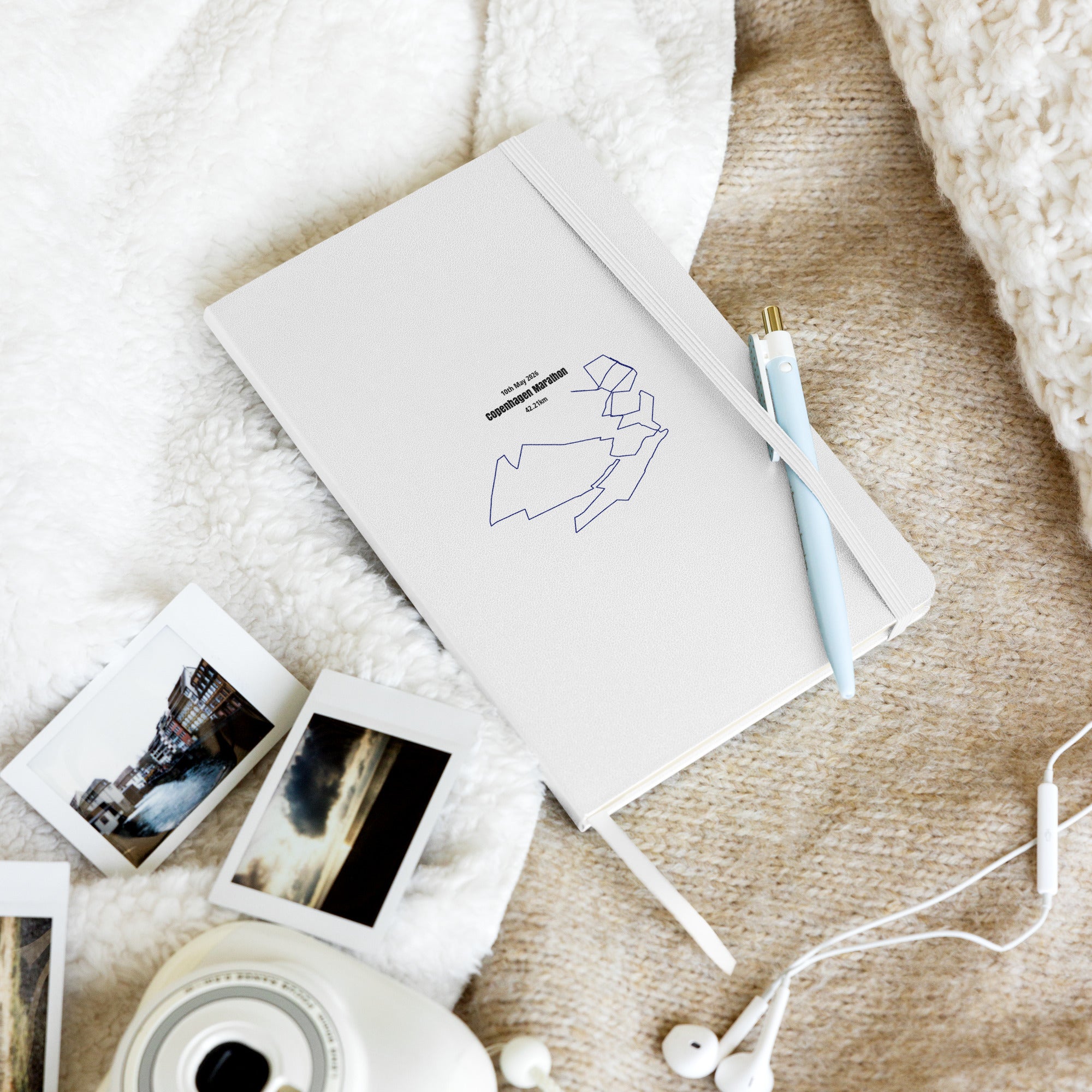 Notebook with custom Strava route print art and a pen, photo album, and photos on a textured surface