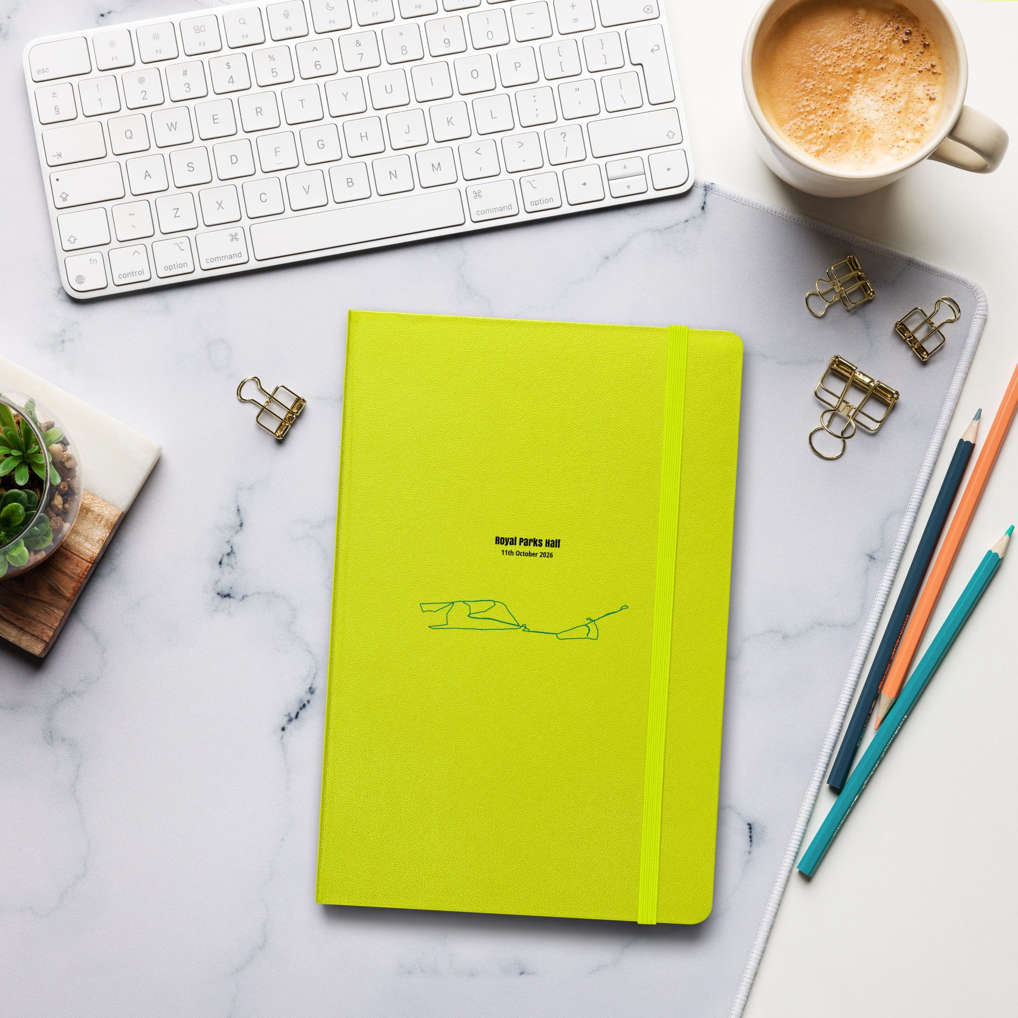 Yellow notebook with custom Strava route print art on a marble desk with office supplies and a cup of coffee