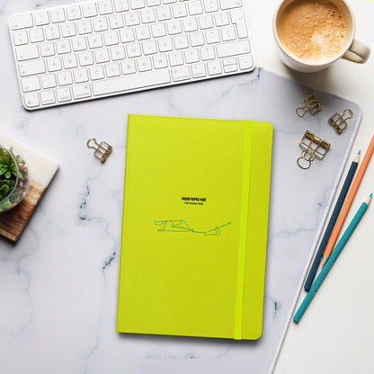 Yellow notebook with custom Strava route print art on a marble desk with office supplies and a cup of coffee