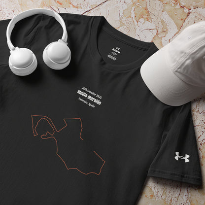 Black t-shirt with a custom Strava route print design and Under Armour logo, accompanied by white headphones and cap on a textured surface