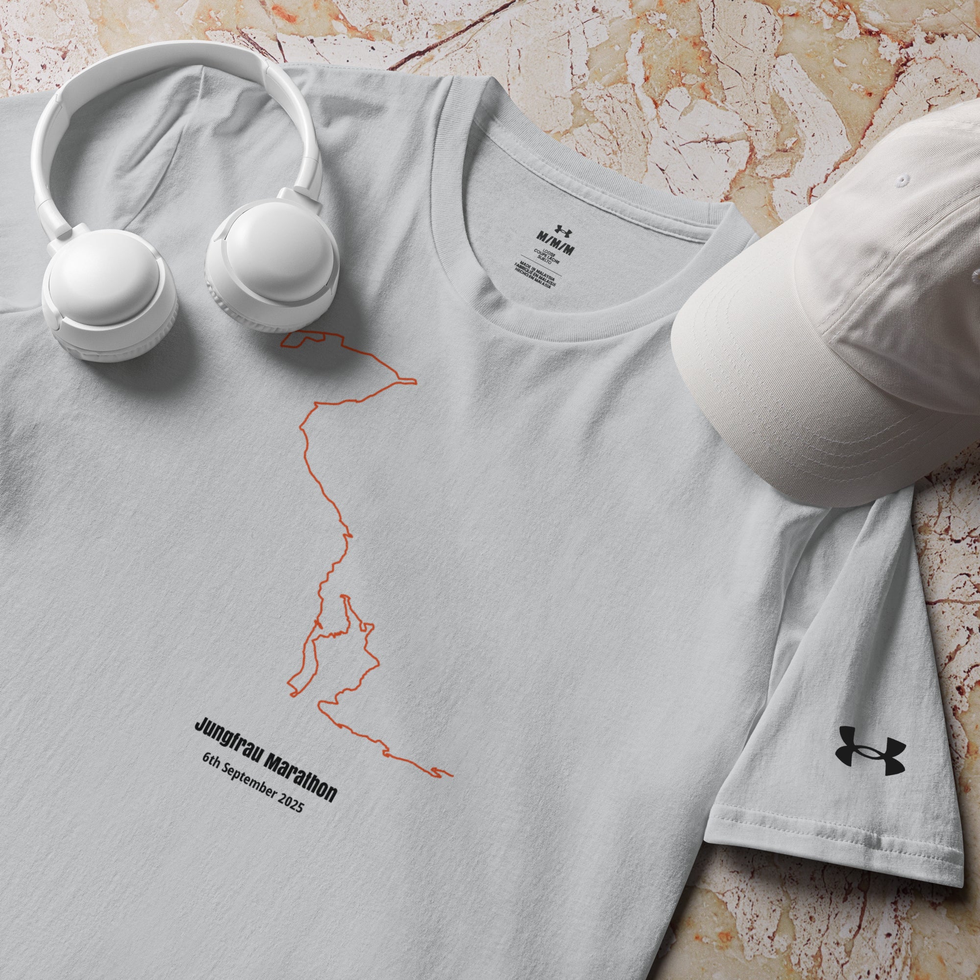 Gray t-shirt with a custom Strava route print design and Under Armour logo, accompanied by white headphones and cap on a marble surface