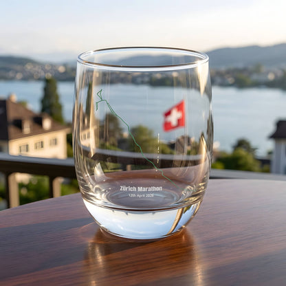 Clear glass with printed custom Strava route art and a flag on a wooden table with a scenic background